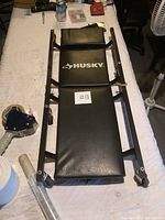 Top and angled views of black Husky branded mechanics creeper, showing padded sections and metal frame with side handles.