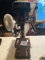 Front view of the Delta Basic Drill Press showing the motor housing, adjustable metal table, lever arm, and power cord.