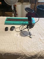 Photo showing Logitech wireless keyboard in box, two wireless mice, and desktop microphone with tripod and pop filter on a table.