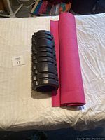 Photo of rolled pink exercise mat and black textured foam roller on a bed.