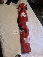 Image of the folded camping chair inside its red carry bag with white maple leaf pattern, laid out on a bed.