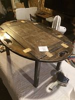 Oval folding wooden serving table shown fully opened on table surface with visible metal hinges and carry handles.