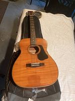 Full body view of acoustic guitar on a soft case, showing natural wood grain finish and six strings.