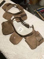 Photo showing two soft brown leather tool belts laid flat, highlighting multiple pockets, pouches, and wide elastic and fabric adjustable waist straps
