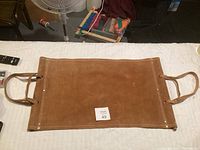 Top view of the new leather wood carrier showing the brown leather surface with stitching and handles on each side.
