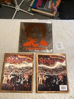 Top-down photo showing the metal artwork with an orange silhouette and two Rolling Stone Special Collectors Edition magazines side by side on a white background.