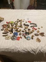 Overview of assorted military pins, badges, and buttons spread out on a white surface with some papers and packaging in the background.