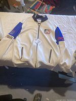 Full view of white Polo Ralph Lauren sailing jacket with black trim, zippered pockets, blue panels on sleeves, and sailing themed logos and embroidery.