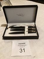 Opened black box showing Sigma branded interior and three black pens with gold accents laid out inside.