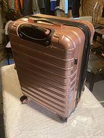 Side view of rose gold hard shell suitcase showing ribbed design and spinner wheels.