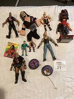 Photo showing 11 assorted wrestling figures and related memorabilia items laid out on fabric surface, including plush doll, small action figures, bust sculpture, card and yo-yo.