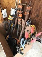 Box containing assorted clamps including large pipe clamps with orange frames, Quick Grip clamps, and C clamps showing age and wear.