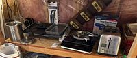 Wooden shelf with various kitchen appliances including Rival Snow Cone Maker in box, two slice toaster, George Foreman grill, Salton electric burner and can crusher.
