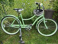 Full side view of the light green ladies bicycle with basket mounted on front and helmet hanging from handlebars with pump standing beside the bike.
