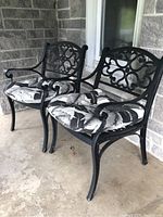 Two matching black metal outdoor chairs with cushions displayed on porch