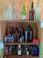 Wide view of wooden shelving unit holding an assortment of clear, amber, green, and cobalt blue bottles including soda, beer, liquor, and medicinal types.