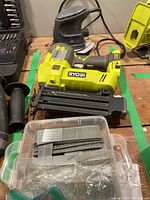 Photo showing Ryobi brad nailer, detachable handle, and container with various brad nails.