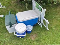 Photo showing variety of coolers, folding table, and folding chair placed on grass.