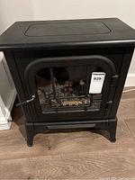 Front view of small black metal electric fireplace heater with glass door and artificial logs inside.