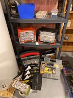 View of shelves displaying various storage boxes with screws, nails, and containers of hardware, along with boxes of light bulbs and some tools on the floor.