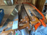 Lot of five hand saws arranged on a wooden surface showing wooden and orange handles with blades varying in size.