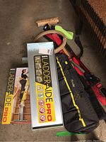 Photo shows Ideal Ladder-Aide Pro metal ladder platform, carrying case, vehicle snow brushes, push broom and steering wheel cover on garage floor.