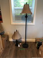 Full view of the matching metal floor lamp and table lamp side by side against a wall with window blinds, shows relative sizing and shade details.