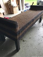 View of the entire rattan bench showing its two-tone woven pattern and metal legs from an angled perspective.
