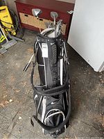 Full view of black Nike golf bag standing upright showing multiple left handed clubs inside, bag has shoulder strap, storage pockets, and built-in stand.