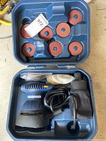 Open blue plastic carrying case containing Mastercraft ARC sander/polisher with attached dust bag, electrical cord, replacement sanding discs and white polishing pads in plastic bags.