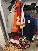 Photo showing hanging jackets, jerseys, and other clothing including heavy coat, Weatherproof jacket, and patterned bags on floor