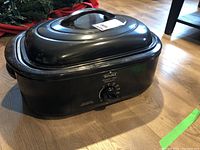 Black Rival roaster oven with lid on, temperature control knob visible on front side, sitting on floor.