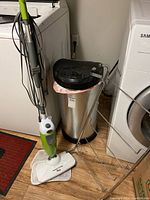 Floor steamer, garbage can and over-the-door rack beside laundry appliances