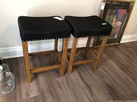Two wooden stools side by side against a wall on wood floor, showing overall condition and design