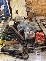 Photo showing hand tools including hammers, screwdrivers, boxes of screws and nails, and miscellaneous small parts on a table.