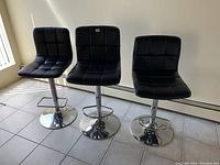 Three black faux leather barstools with chrome bases positioned side by side showing the different sizes and footrests.