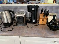 Overview of Black & Decker electric kettle, stainless steel toaster, coffee maker, Zwilling knife block with knives, and black ceramic tea kettle on kitchen counter.