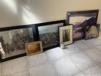 Six framed pictures and one framed clock arranged on a tiled floor showing size and variety of lot items.