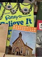 Photo of various vintage books closely grouped showing titles including Ripley's Believe It or Not, Barkerville guide, and others.