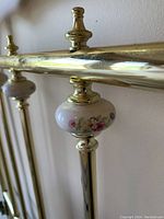 Close-up of brass tubing with attached white porcelain finial featuring hand-painted pink and yellow flowers