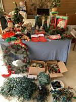Full view of assorted Christmas decorations spread on table including wreaths, stockings, ornaments, and trees.