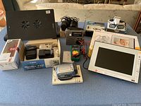 Wide view of entire electronics lot showing Canon camera, Kodak digital frame, radio, laptop stand, multimeter and speakers