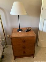 Wooden 3 drawer end table with black metal lamp on top.