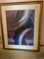 Front view of framed abstract art print with gold-tone frame, visible white matting, and multi-colored abstract design dominated by purples and blues.