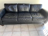 Front view of black leather couch showing three seat cushions and slight wear.