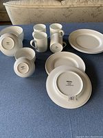 Multiple white dinnerware pieces including mugs, bowls, and plates arranged on a blue surface.