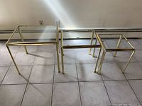 Three brass and glass nesting tables arranged side by side on tile floor, showing size difference and design