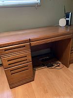 Front view of oak desk showing top surface, drawer pedestal with three drawers, and kneehole space on the right.