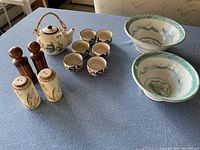 Overview of whole set on table showing two painted pottery bowls, Chinese tea set with teapot and five cups, and two pairs of ceramic salt and pepper shakers.