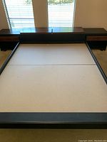 Queen size bed frame with headboard and two end tables against a window.